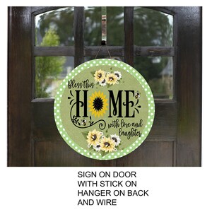 A round sign with the text "Bless this home with love and laughter" hanging on a door, with a floral design and a sunflower motif.
