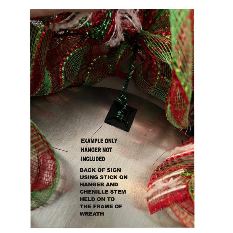 May include: Close-up of a Christmas wreath with red, green, and white mesh. A black square hanger is attached to the wreath. Text on the image reads: "EXAMPLE ONLY HANGER NOT INCLUDED BACK OF SIGN USING STICK ON HANGER AND CHENILLE STEM HELD ON TO THE FRAME OF WREATH."