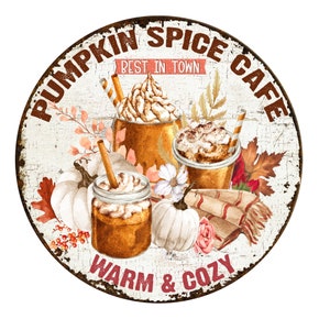 K&ouml;nnte beinhalten: Ein rundes Metallschild mit wei&szlig;em Hintergrund und braunen, abgenutzten R&auml;ndern. Das Schild zeigt ein rustikales Design mit dem Text "Pumpkin Spice Cafe" in braunen Buchstaben. Der Text "Best in Town" ist in Pink auf einem wei&szlig;en Banner geschrieben. Das Schild zeigt au&szlig;erdem eine Aquarell-Illustration von drei Pumpkin Spice Lattes mit Schlagsahne und Zimt, sowie K&uuml;rbissen, Herbstbl&auml;ttern und einer gem&uuml;tlichen Decke. Der Text "Warm & Cozy" ist in braunen Buchstaben am unteren Rand des Schildes geschrieben.