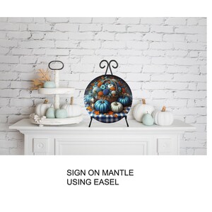 A decorative arrangement of pumpkins and fall foliage on a white mantelpiece, with a sign that reads "SIGN ON MANTLE USING EASEL".