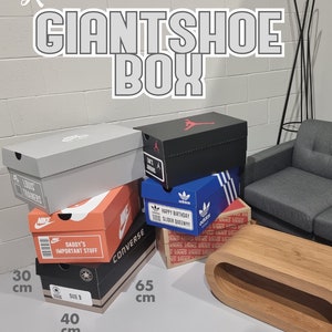 May include: A stack of shoe boxes of various sizes and brands, including Nike, Converse, Adidas, and Vans. The boxes are stacked on a white surface with measurements in centimetres. The boxes are labelled with various text, including "Daddy's Important Stuff", "Happy Birthday Slider Queen!!!", and "Size 9".