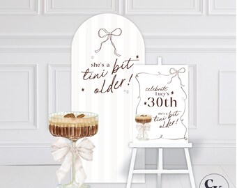 May include: A sign and easel with the text "she's a tini bit older!" and "celebrate Lucy's 30th". A cocktail with a white bow is also featured. The background is white with vertical stripes.