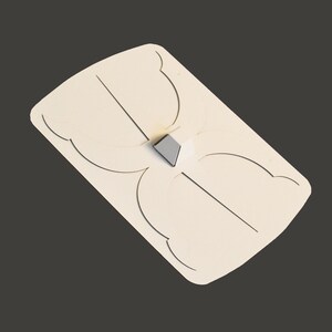 May include: A white wooden shield with a cut-out design. The shield has a small, grey, triangular piece attached to the centre.