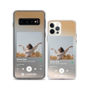May include: Two clear phone cases with a gradient background from light brown to white. The cases feature a photo of a person with arms outstretched in a field of yellow flowers. The phone cases have a music player interface with the song "Show Out" by Kid Cudi, Skepta, and Pop Smoke playing.