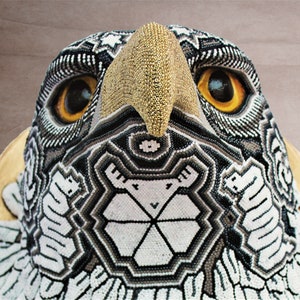 May include: Close-up of a beaded eagle head sculpture with a gold beak and black, white, and gray geometric patterns.