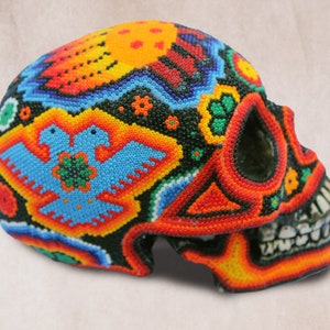 May include: A colorful beaded skull with a detailed design of two birds and flowers. The skull is made of black beads with red, orange, yellow, blue, and green accents.