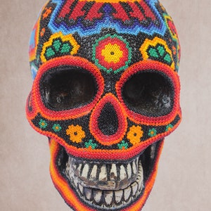May include: A colorful beaded skull with a black background and red, orange, yellow, green, and blue beads. The skull has a detailed design with flowers and geometric patterns.