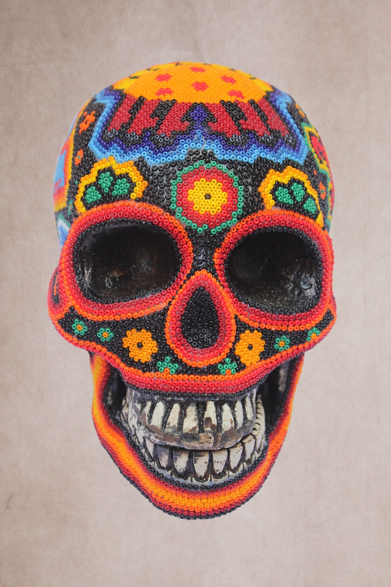 May include: A colorful beaded skull with a black background and red, orange, yellow, green, and blue beads. The skull has a detailed design with flowers and geometric patterns.