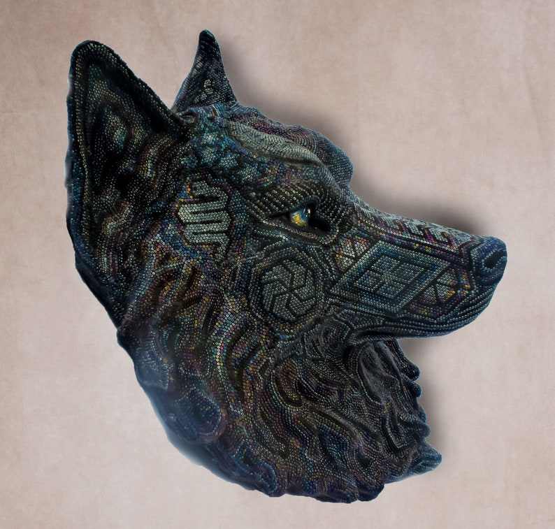 Detailed beaded wolf head sculpture featuring intricate patterns in vibrant shades of blue, green, and purple. The wolf’s striking green eyes create a captivating focal point. Handcrafted with glass seed beads, this textured and dimensional piece brings depth and brilliance to any space. Perfect as wall decor, this Huichol (Wixárika)-inspired artwork blends Mexican folk art, spiritual symbolism, and artisan craftsmanship—ideal for collectors and lovers of unique handmade decor.
