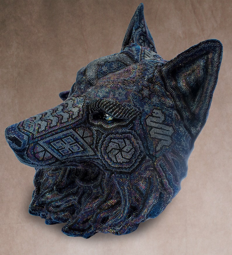 Detailed beaded wolf head sculpture featuring intricate patterns in vibrant shades of blue, green, and purple. The wolf’s striking green eyes create a captivating focal point. Handcrafted with glass seed beads, this textured and dimensional piece brings depth and brilliance to any space. Perfect as wall decor, this Huichol (Wixárika)-inspired artwork blends Mexican folk art, spiritual symbolism, and artisan craftsmanship—ideal for collectors and lovers of unique handmade decor.