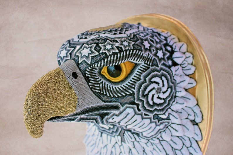 May include: A beaded eagle head sculpture with a gold beak and a detailed eye. The eagle's feathers are white and gray with intricate geometric patterns.