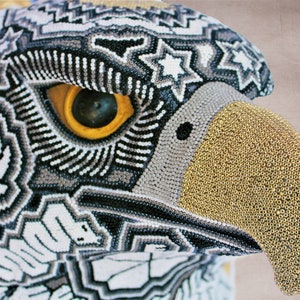 May include: Close-up of a beaded eagle head with a black, white, and gray patterned design. The beak is made of gold beads.