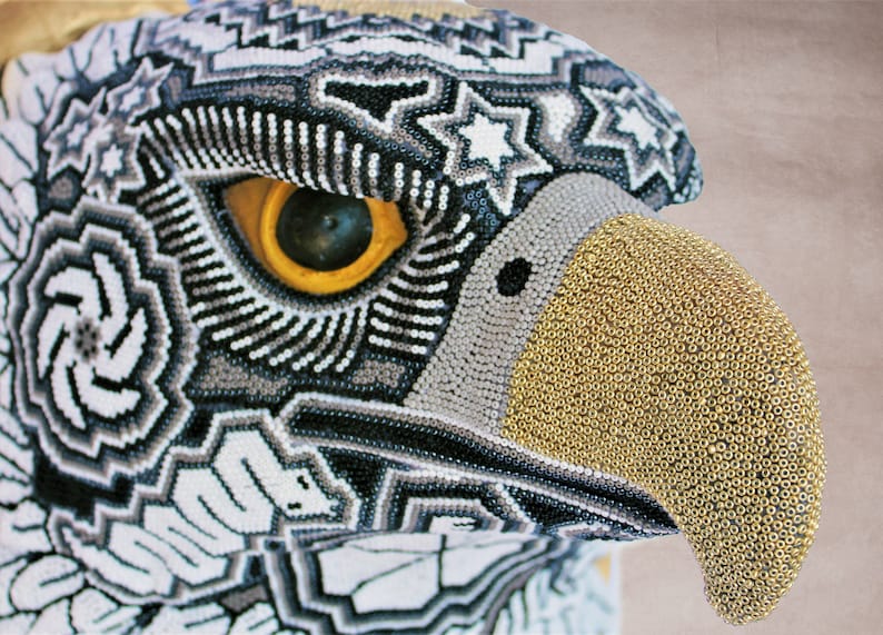 May include: Close-up of a beaded eagle head with a black, white, and gray patterned design. The beak is made of gold beads.