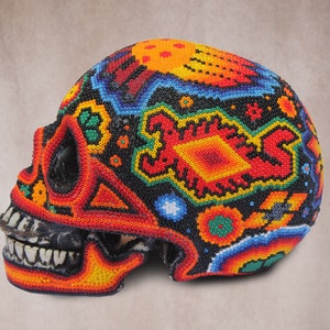 May include: A colorful skull made of beads. The skull is decorated with a variety of geometric and floral patterns in shades of red, orange, yellow, green, blue, and black.