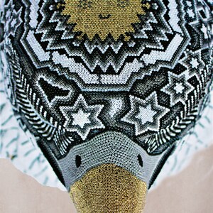 May include: A beaded eagle head sculpture with a black, white, and gold geometric pattern. The eagle's beak is gold and the eyes are black.