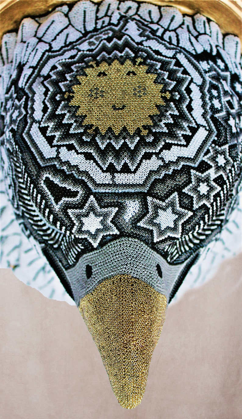 May include: A beaded eagle head sculpture with a black, white, and gold geometric pattern. The eagle's beak is gold and the eyes are black.