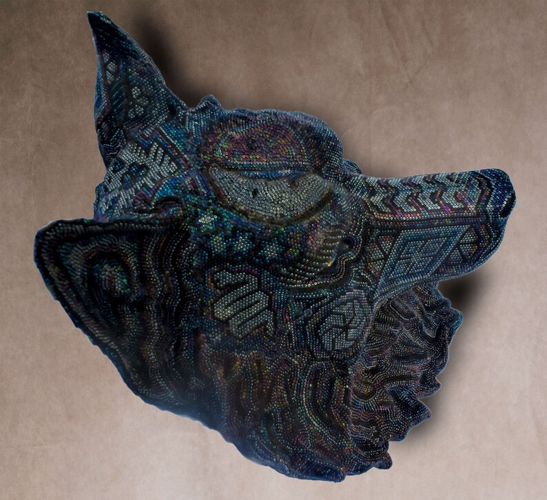 Detailed beaded wolf head sculpture featuring intricate patterns in vibrant shades of blue, green, and purple. The wolf’s striking green eyes create a captivating focal point. Handcrafted with glass seed beads, this textured and dimensional piece brings depth and brilliance to any space. Perfect as wall decor, this Huichol (Wixárika)-inspired artwork blends Mexican folk art, spiritual symbolism, and artisan craftsmanship—ideal for collectors and lovers of unique handmade decor.