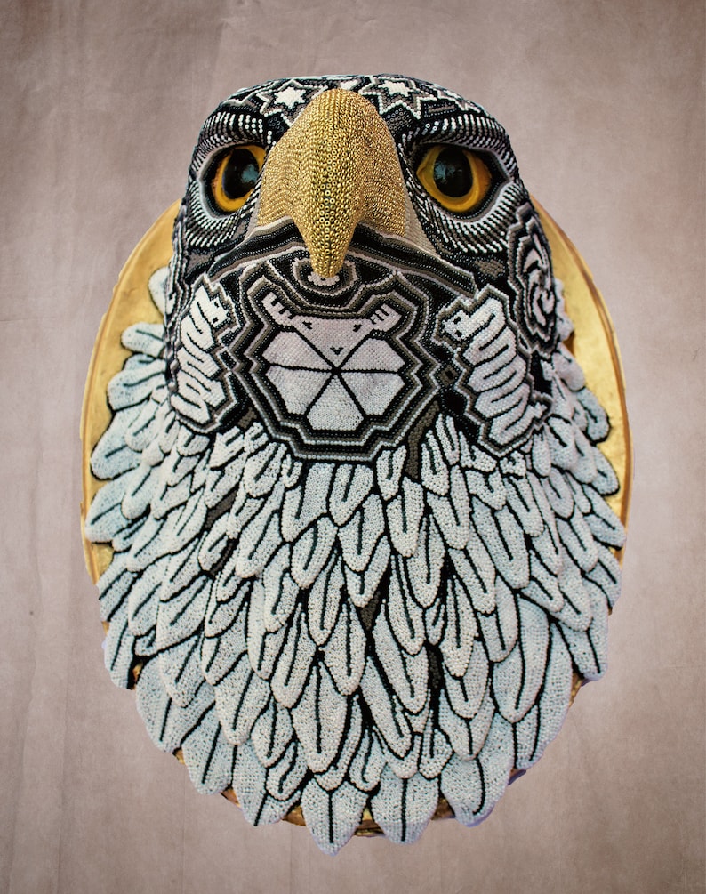 May include: A beaded eagle head sculpture with a gold beak and black and white geometric patterns. The eagle's head is mounted on a gold circular base.