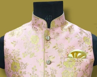 May include: A pink and gold floral patterned waistcoat with a mandarin collar and button closure. The waistcoat has a pocket on the right side and a gold trim around the edges.