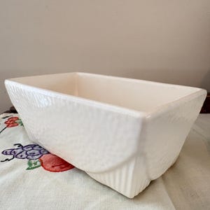 Puede incluir: Una taza de cerámica blanca con un asa negra y el texto "But First, Coffee" en negro, con una fuente de estilo manuscrito. La taza está sobre una superficie blanca.