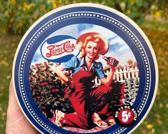 May include: A round metal Pepsi-Cola sign featuring a woman in red overalls and a blue shirt kneeling in a garden, holding a bottle. The sign includes the Pepsi-Cola logo, a white picket fence background, and a red circle text reading Big 12 Oz. Bottle 5 cents.