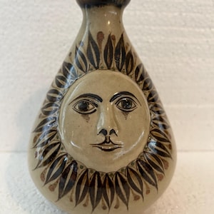 A vintage pottery art vase signed by Carlos Villanueva depicting a raised Sun Face image on one side with stylized Foliage Art on the other.