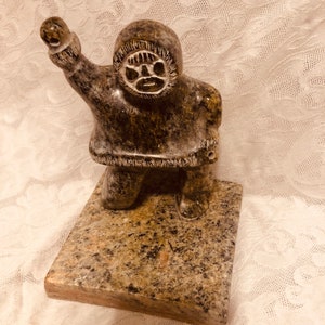 A well executed inuit soapstone figure on a plinth. Some items from the sculpture are missing from the hands and base. The soapstone signed.