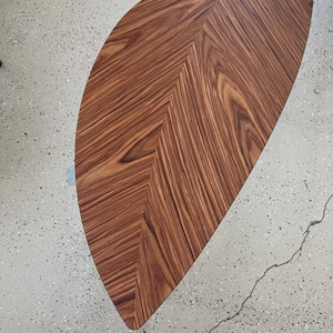 May include: A half-moon shaped wooden table with a rich, warm brown finish. The tabletop features a chevron pattern, with the wood grain running in parallel lines. The table's design is simple and elegant, suitable for various interior styles.