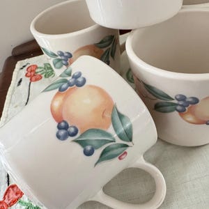 5 vintage Corning mugs in the Abundance pattern of peaches, blueberries, cherries, green leaves on white background, preowned in good shape