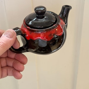 May include: A small, ceramic teapot with a glossy black finish and a vibrant red band. The teapot features a lid, handle, and spout, all in black. The design is a striking contrast of colors and textures, perfect for tea lovers.