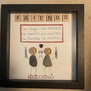 May include: A framed artwork with the word "FRIENDS" spelled out in letter tiles. The artwork features a hand-drawn illustration of two figures with wine glasses, and the text "Our laughs are limitless. Our memories are countless. Our friendship is endless."  The artwork is signed "GAYLE + ANDREA".