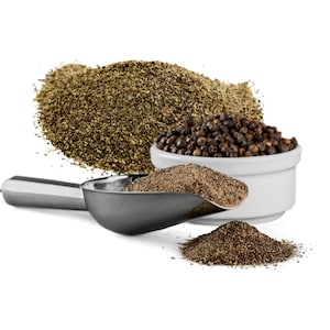 Op de afbeelding: Een witte kom gevuld met zwarte peperkorrels, een metalen schep gevuld met gemalen zwarte peper en een hoop gemalen zwarte peper op een witte achtergrond.