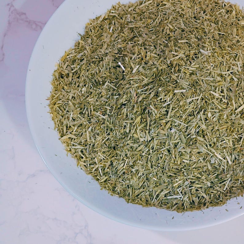 May include: A white plate filled with dried, chopped green herbs. The herbs have a light green and tan color, with a texture of small, thin pieces. The plate is set against a white and gray marble surface.