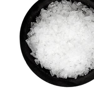 May include: A close-up of a black bowl filled with white, coarse sea salt crystals.