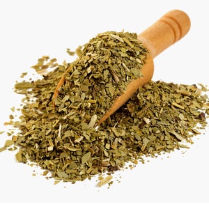 Peut inclure: Une cuillère en bois remplie de feuilles de yerba maté vertes et séchées, se déversant sur une surface blanche. Les feuilles sont de tailles et de textures variées, avec un aspect naturel et terreux. La cuillère est en bois clair.