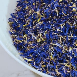 Könnte beinhalten: Eine Schüssel gefüllt mit getrockneten blauen Kornblumenblütenblättern und gelben Blütenblättern. Die Blütenblätter sind eine Mischung aus hell- und dunkelblau.