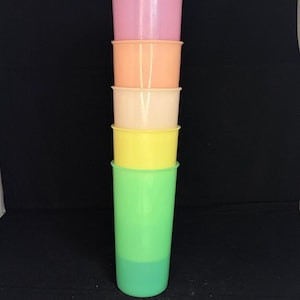 Puede incluir: Una pila vertical de cinco vasos cilíndricos de plástico en un degradado de colores. El vaso superior es rosa claro, seguido de melocotón, crema, amarillo y un vaso base de color verde lima brillante. Cada vaso tiene un acabado liso y un borde.