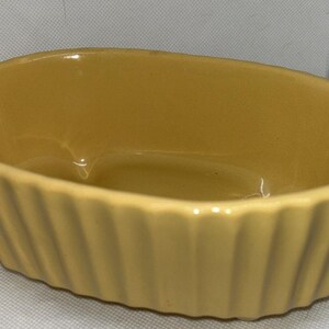 Puede incluir: Una fuente ovalada de cerámica amarilla con exterior acanalado. El plato tiene un acabado brillante y está vacío. Los lados acanalados añaden un toque decorativo a este utensilio de cocina funcional.