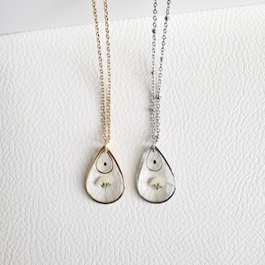 Pu&ograve; includere: Due delicate collane con ciondoli a forma di lacrima. Ogni ciondolo contiene un fiore bianco pressato e un piccolo punto nero. Una collana ha una catena dorata e l'altra una catena argentata.