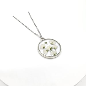 May include: A silver chain necklace with a round pendant featuring a bouquet of white flowers pressed inside clear resin.