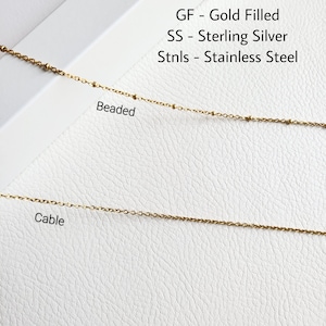 May include: Close-up of two gold-colored chain necklaces. The top necklace is beaded, and the bottom is a cable chain. Text in the image reads: GF - Gold Filled, SS - Sterling Silver, Stnls - Stainless Steel.
