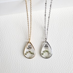 Pu&ograve; includere: Due delicate collane con ciondoli a forma di goccia che presentano fiori secchi pressati e semi neri. Una collana ha una catena dorata e l'altra una catena argentata.