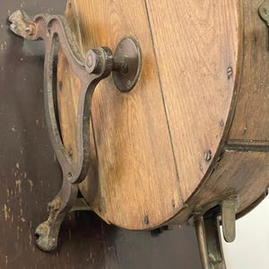 May include: Antique wooden butter churn with metal hardware. The churn features a round wooden barrel with metal bands and a crank handle. The base is dark brown, and the metal has a rustic appearance.