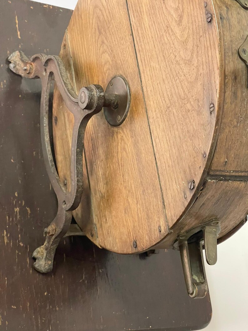 May include: Antique wooden butter churn with metal hardware. The churn features a round wooden barrel with metal bands and a crank handle. The base is dark brown, and the metal has a rustic appearance.