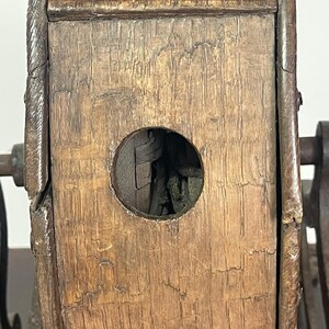May include: Close-up of a weathered wooden object with a circular opening. The wood has a rich, aged appearance with visible grain and texture. Metal components are attached to the wooden structure, suggesting a mechanical or functional purpose. The object's design hints at vintage craftsmanship.