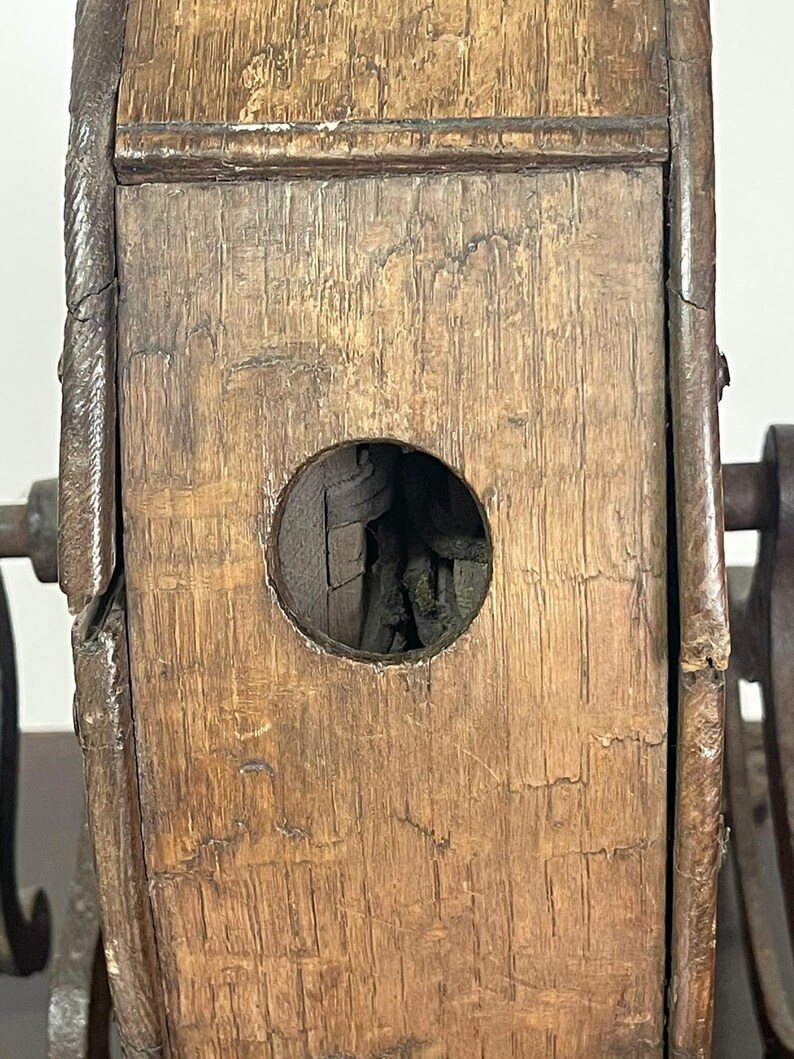 May include: Close-up of a weathered wooden object with a circular opening. The wood has a rich, aged appearance with visible grain and texture. Metal components are attached to the wooden structure, suggesting a mechanical or functional purpose. The object's design hints at vintage craftsmanship.