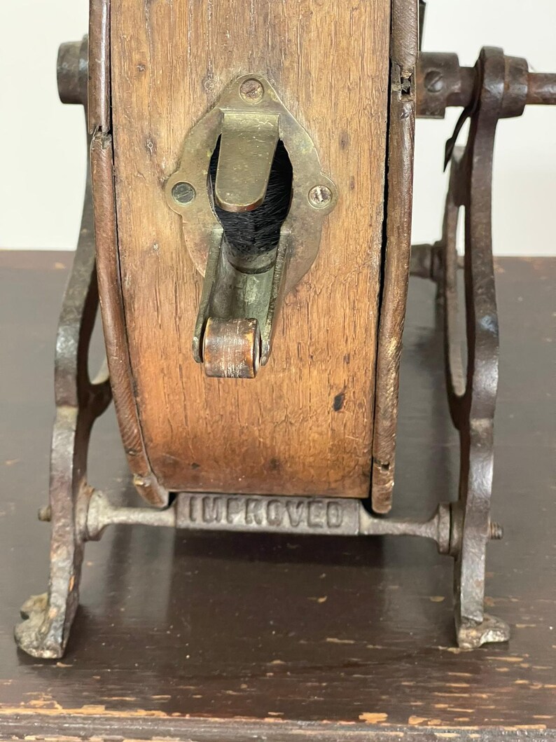 May include: Close-up of an antique wooden and metal object. The wooden portion is rectangular with a brass fitting and a dark opening. The metal frame is dark and has the word "IMPROVED" stamped on it. The object appears to be a vintage tool.