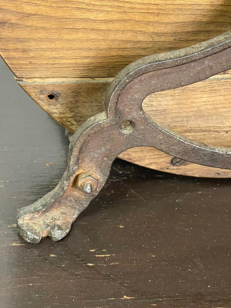 May include: Close-up of a vintage wooden furniture piece with a metal leg. The leg is ornate, with a claw foot design and a rusty, aged appearance. The wood has a natural grain and a warm, light brown color.