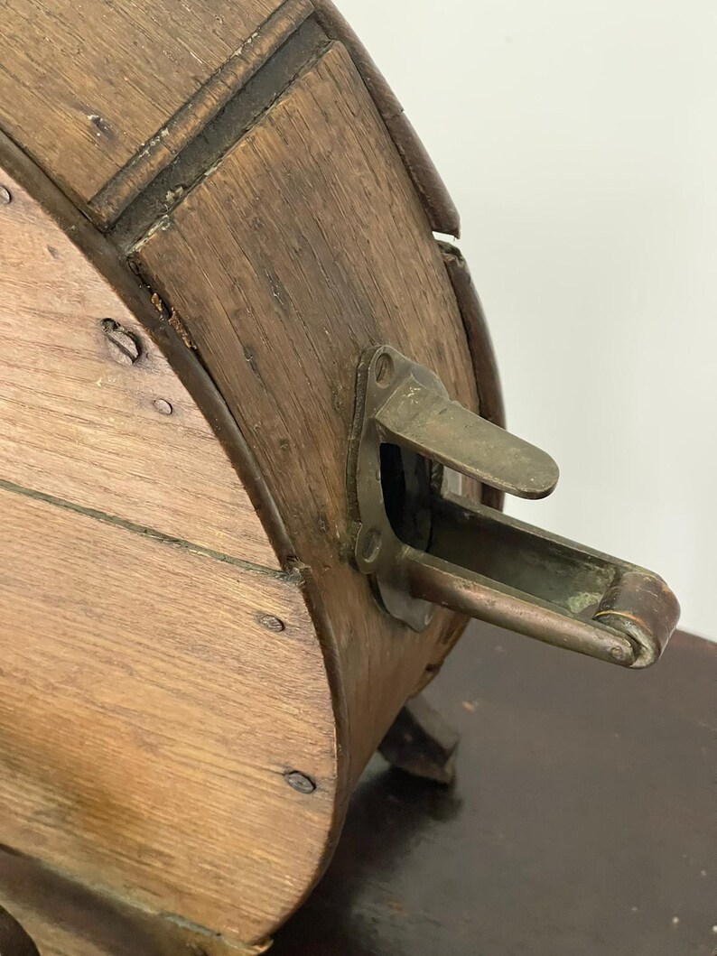 May include: Close-up of an antique wooden barrel with metal hardware. The barrel is made of light brown wood with dark brown accents and metal rivets. A brass-colored metal latch is visible on the side. The barrel is likely used for storage or decoration.