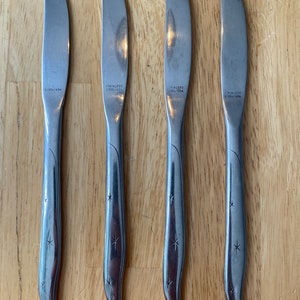 May include: Four silver dinner knives with star-shaped designs on the handles. Each knife has "Stainless Steel USA" engraved on the blade.